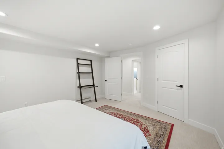 Recessed lighting, smooth white walls, white doors with matte black hardware, and neutral carpet flooring