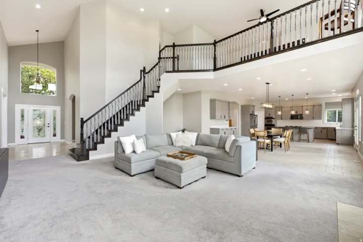 Two-story foyer with an arched window, dual-level staircase with white balusters and dark wood handrails, and an open concept kitchen with light gray cabinetry