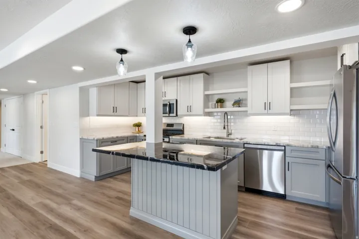 Modern kitchen featuring two-tone cabinetry, stainless steel appliances, black granite island countertop, white subway tile backsplash, and wood-finish flooring