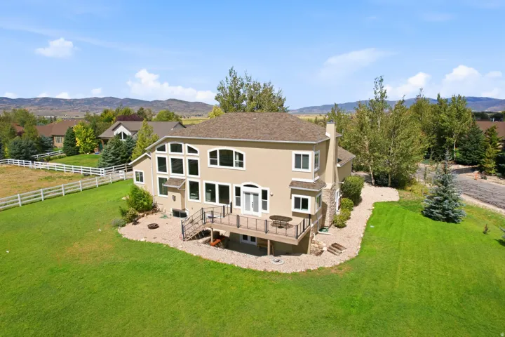 Expansive green lawn, exterior deck, stucco siding, multi-pane windows, and a stone chimney feature