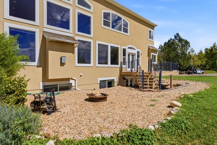 Expansive rear exterior featuring multiple large windows, a raised deck with metal railings, and a ground-level fire pit area