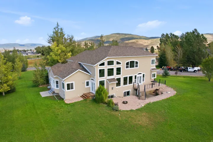 Expansive green lawn surrounding a stucco exterior residence with multiple large windows, a raised outdoor deck, and a lower-level patio area