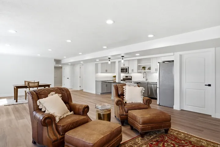 Open-concept living space with wood-finish flooring, recessed lighting, and a full kitchen featuring stainless steel appliances, shaker-style cabinetry, and a subway tile backsplash
