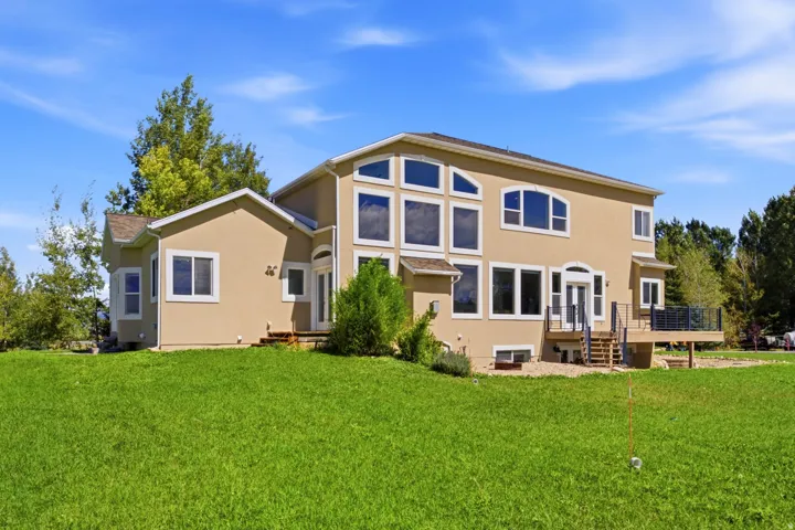 Stucco exterior with multiple window styles, expansive rear decking, a walk-out basement, and a manicured lawn