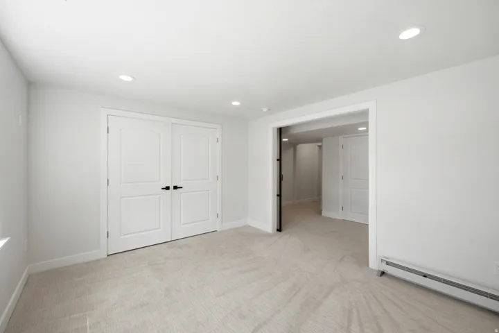 Recessed lighting illuminates the neutral carpeted flooring and white walls