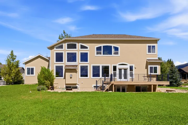 Expansive rear facade featuring a multi-level deck with black railing, large picture windows, and double glass doors