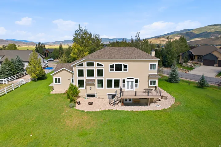 Stucco exterior with a multi-level window arrangement, rear deck with dark railings, and a expansive grassy yard
