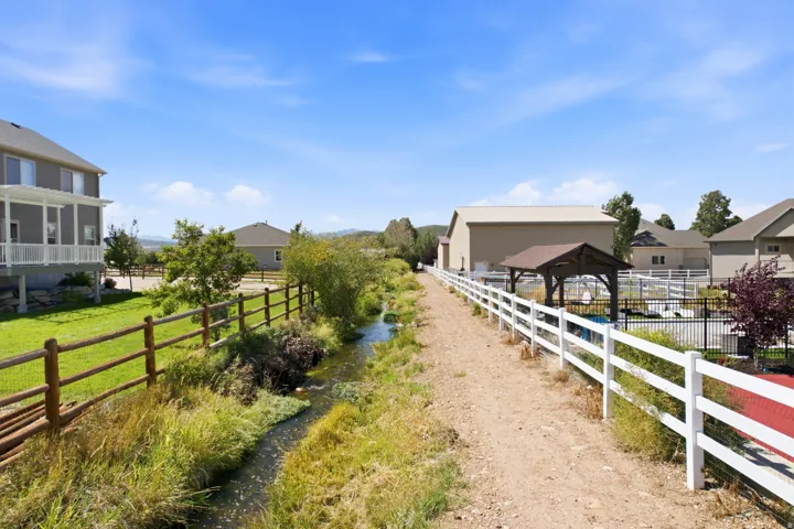 Expansive outdoor area featuring a water channel, wood fencing, white split-rail fencing, a covered outdoor structure, and an adjacent building