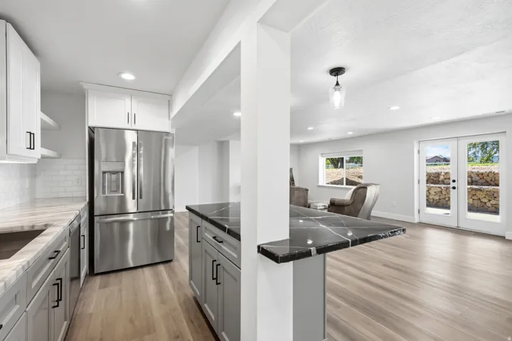 Stainless steel refrigerator, white shaker upper cabinetry, gray shaker base cabinetry, dark stone countertops, and light wood-finish flooring