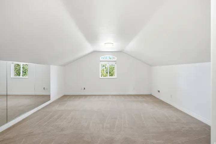 Vaulted ceiling, arched window, wall-to-wall carpeting, mirrored wall, and flush-mount ceiling light fixture