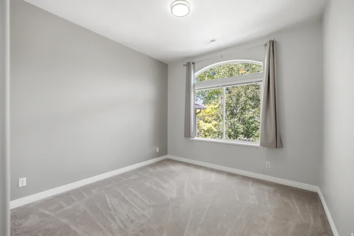 Arched window with ample natural light, neutral-toned walls, and carpeted flooring