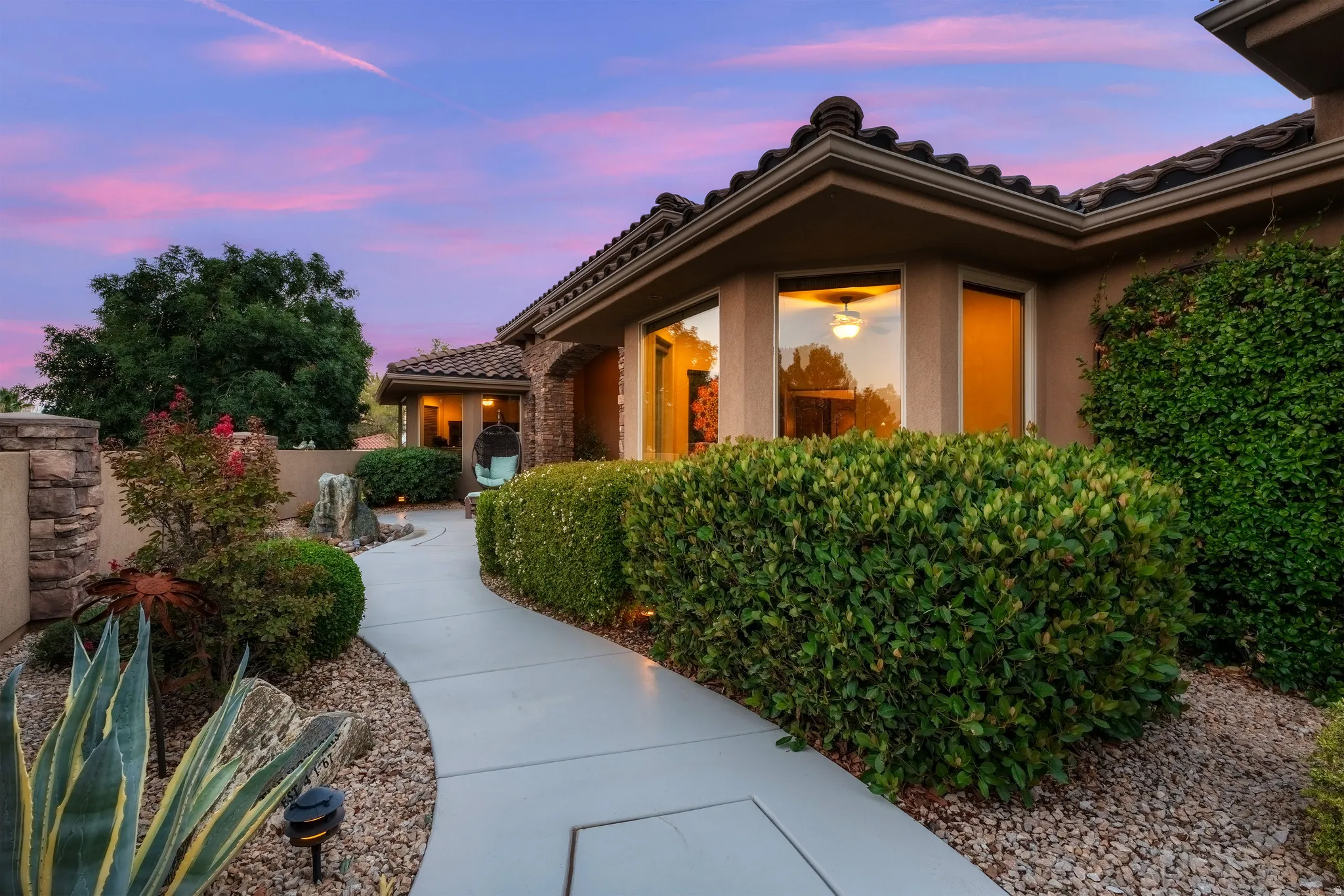 Stucco exterior with a tile roof, featuring a curved walkway, bay window, and extensive shrubbery
