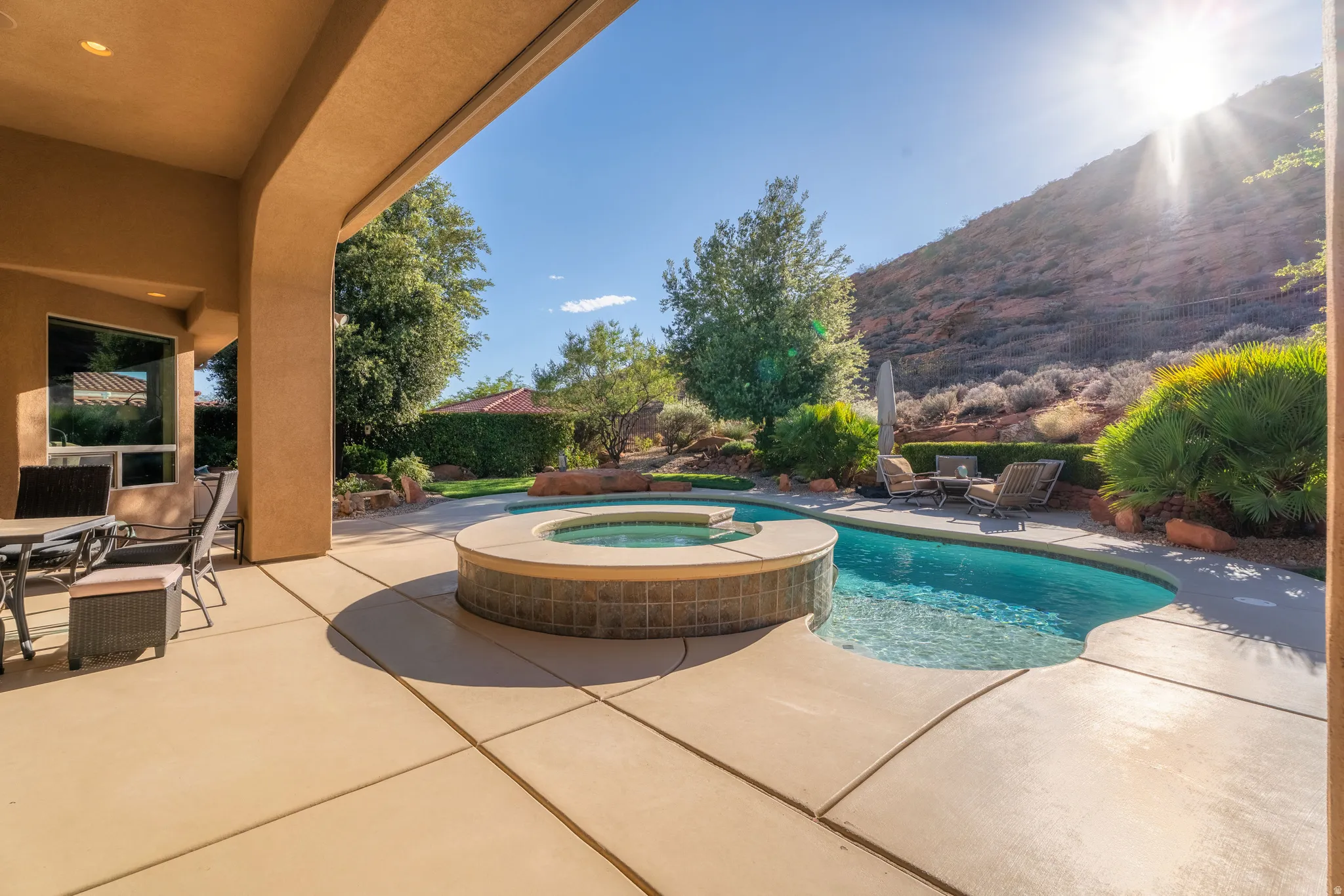 Expansive covered patio featuring a built-in swimming pool and spa, surrounded by mature landscaping and a natural rock formation backdrop