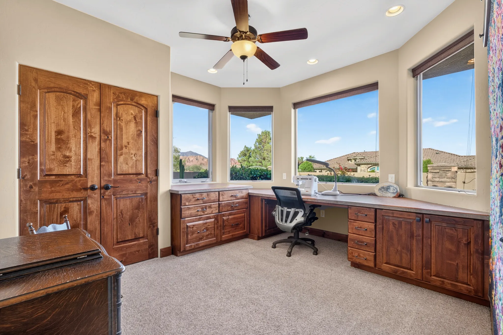 Built-in wood-finish cabinetry with an expansive countertop, featuring large windows, a ceiling fan, recessed lighting, and wood-finish doors
