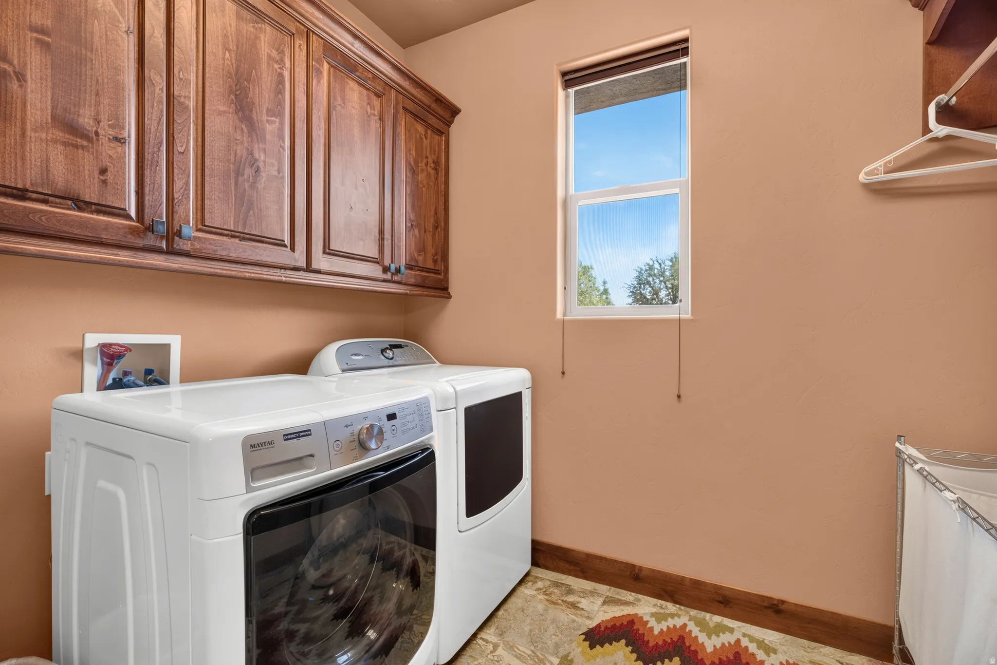 Wood-finish upper cabinetry, window with privacy blind, and tile flooring with wood-finish trim