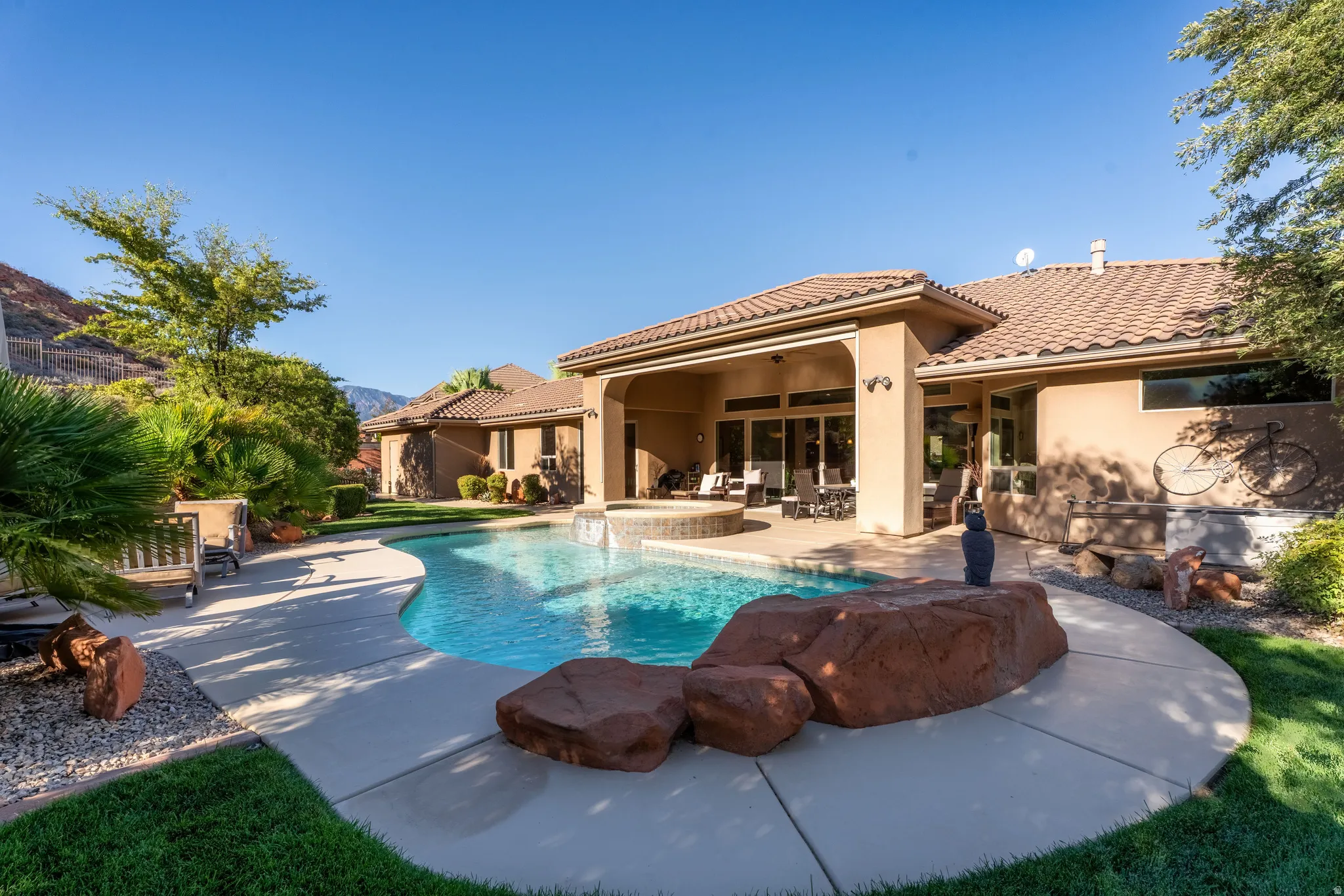 Outdoor swimming pool with integrated spa, expansive concrete patio, covered patio area, and desert landscaping