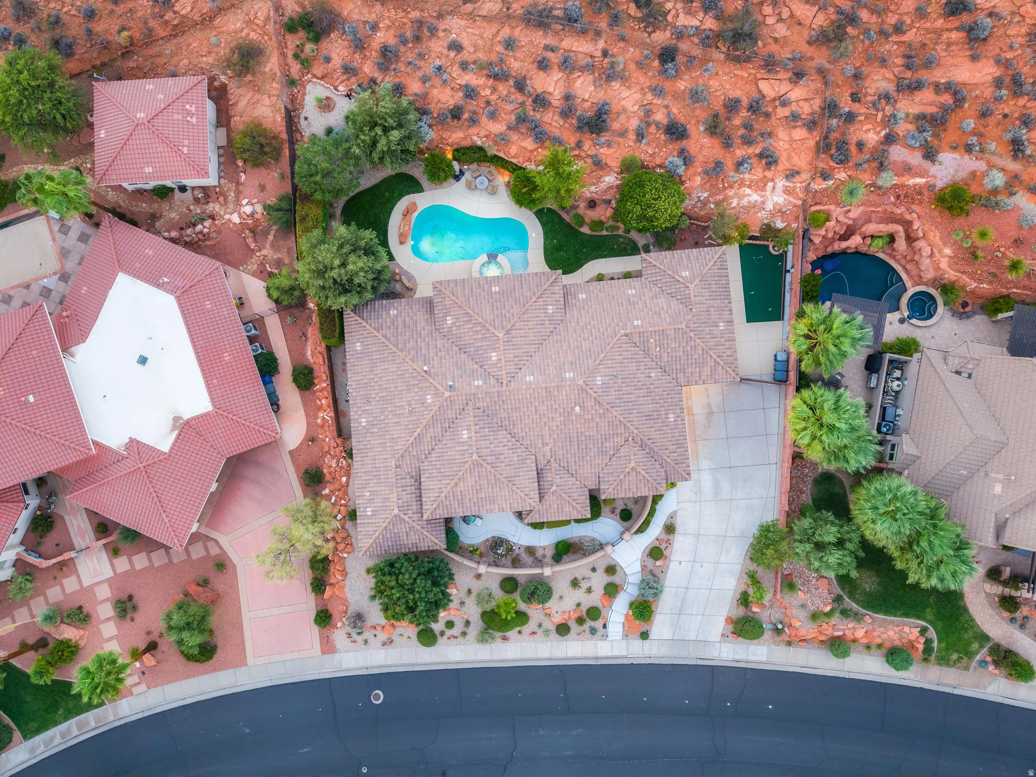 Terracotta tile roofing, expansive paved driveway, sculpted front landscaping, and a curvilinear pool with surrounding patio