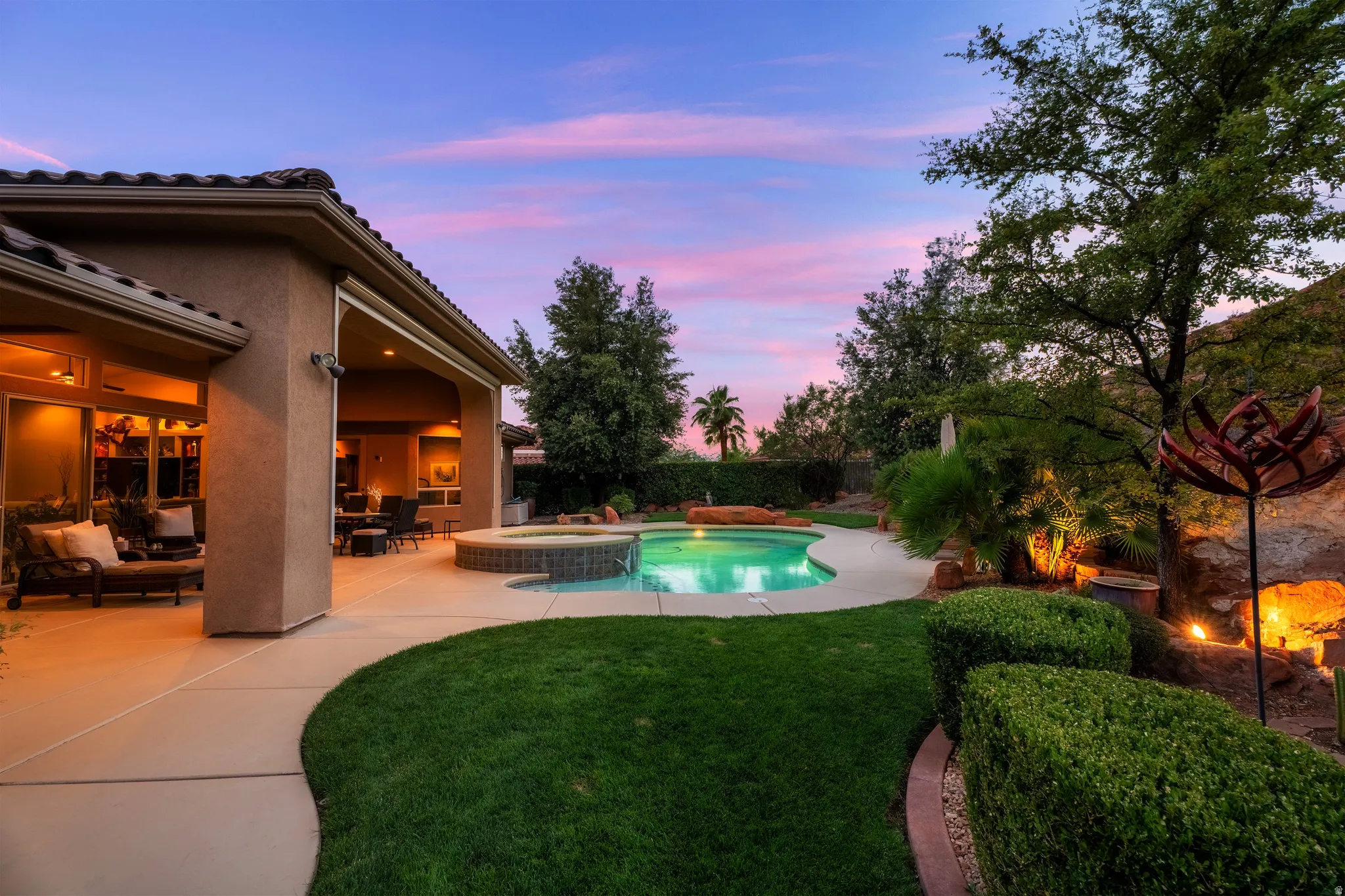 Curved swimming pool with an integrated spa, expansive patio, and manicured lawn