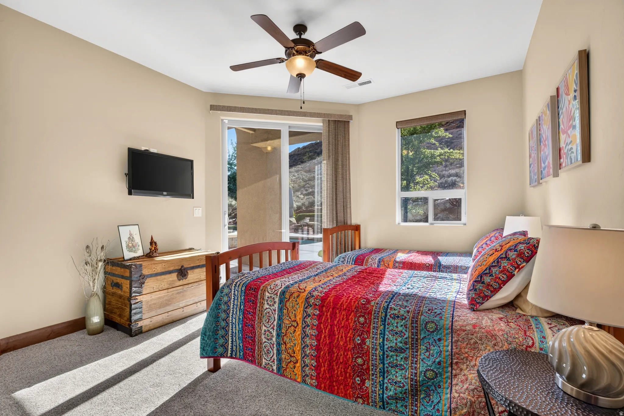 Ceiling fan with integrated lighting, wall-mounted television, sliding glass door, fixed window, and carpeted flooring