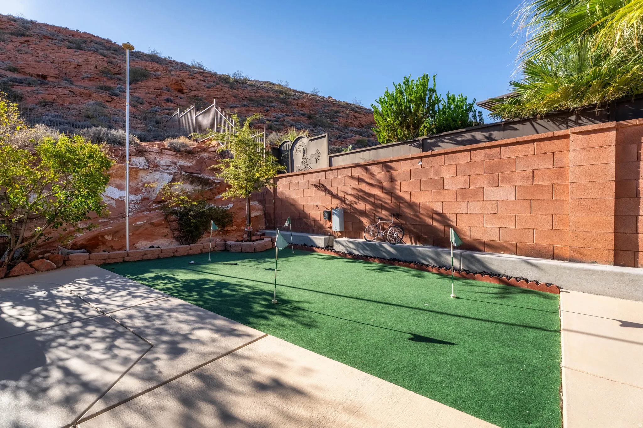 Private putting green, block privacy wall, concrete patio, natural rock landscaping, and mature foliage