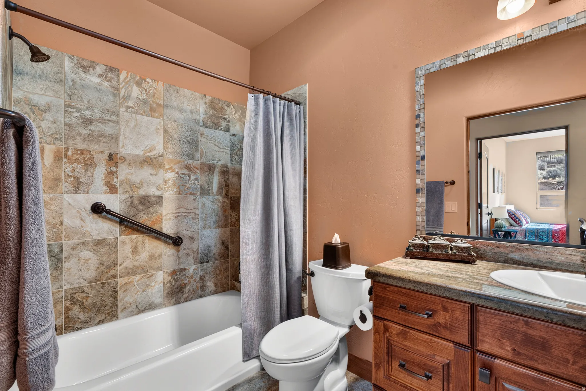 Tub/shower combination with tile surround, wood-finish vanity with countertop, and framed mirror