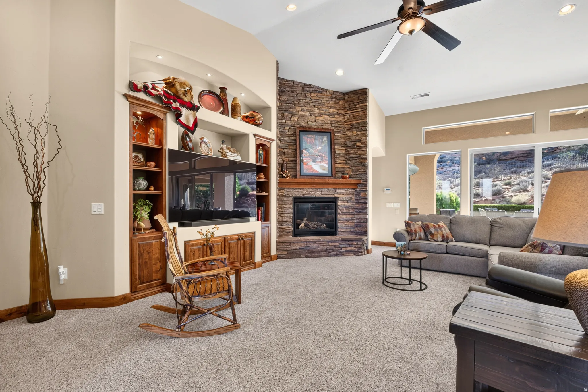 Built-in media center with wood cabinetry, stone-clad fireplace with wood mantel, ceiling fan, recessed lighting, and large windows