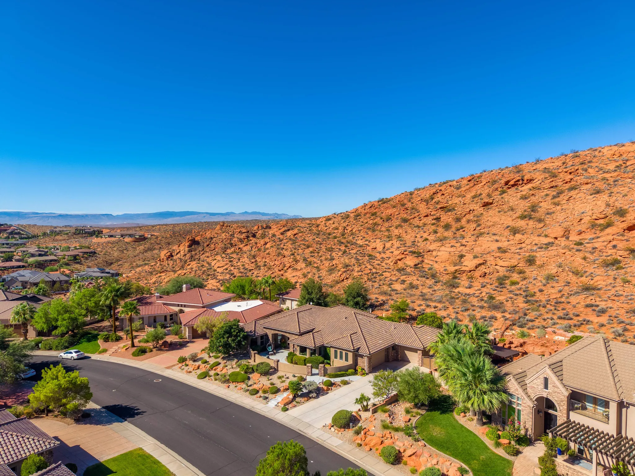 Expansive property featuring a tiled roof, stucco exterior, multiple garages, and a paved driveway, set against a rocky hillside backdrop