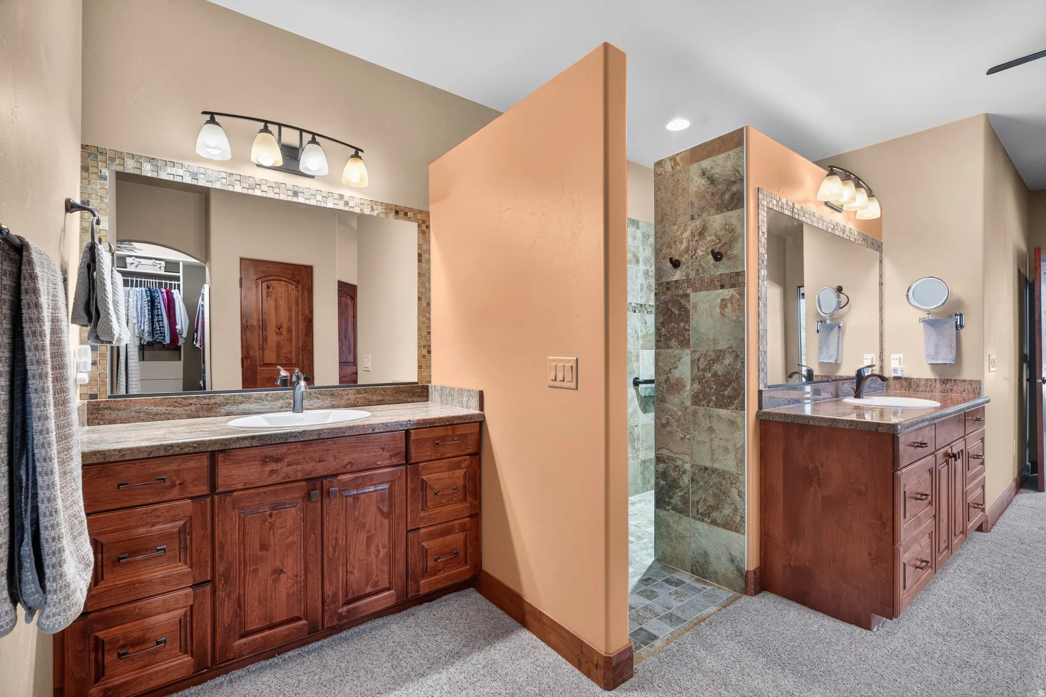 Dual vanity with warm wood-finish cabinetry, stone-look countertops, and integrated sinks