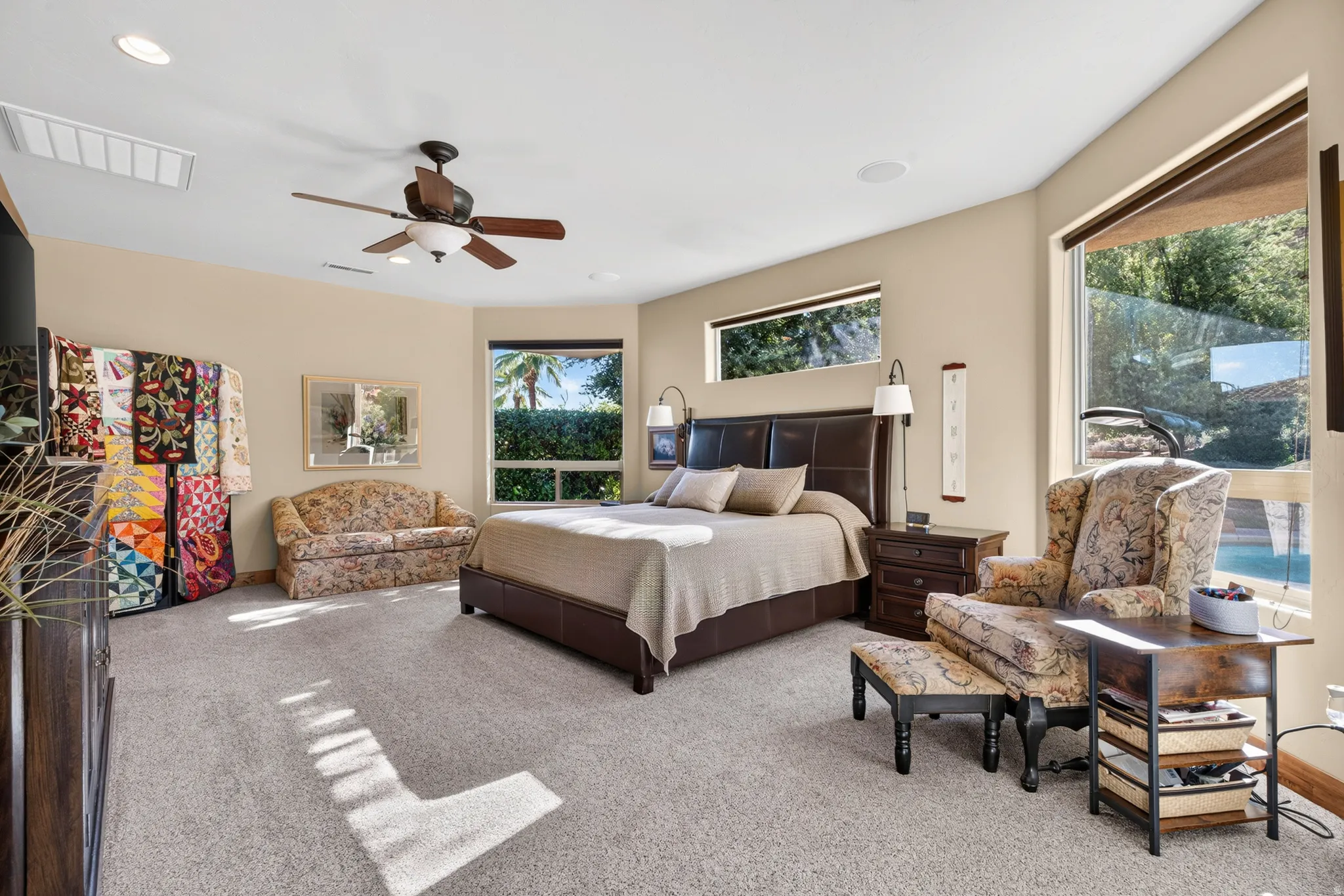 Spacious carpeted room featuring a ceiling fan, recessed lighting, and multiple windows