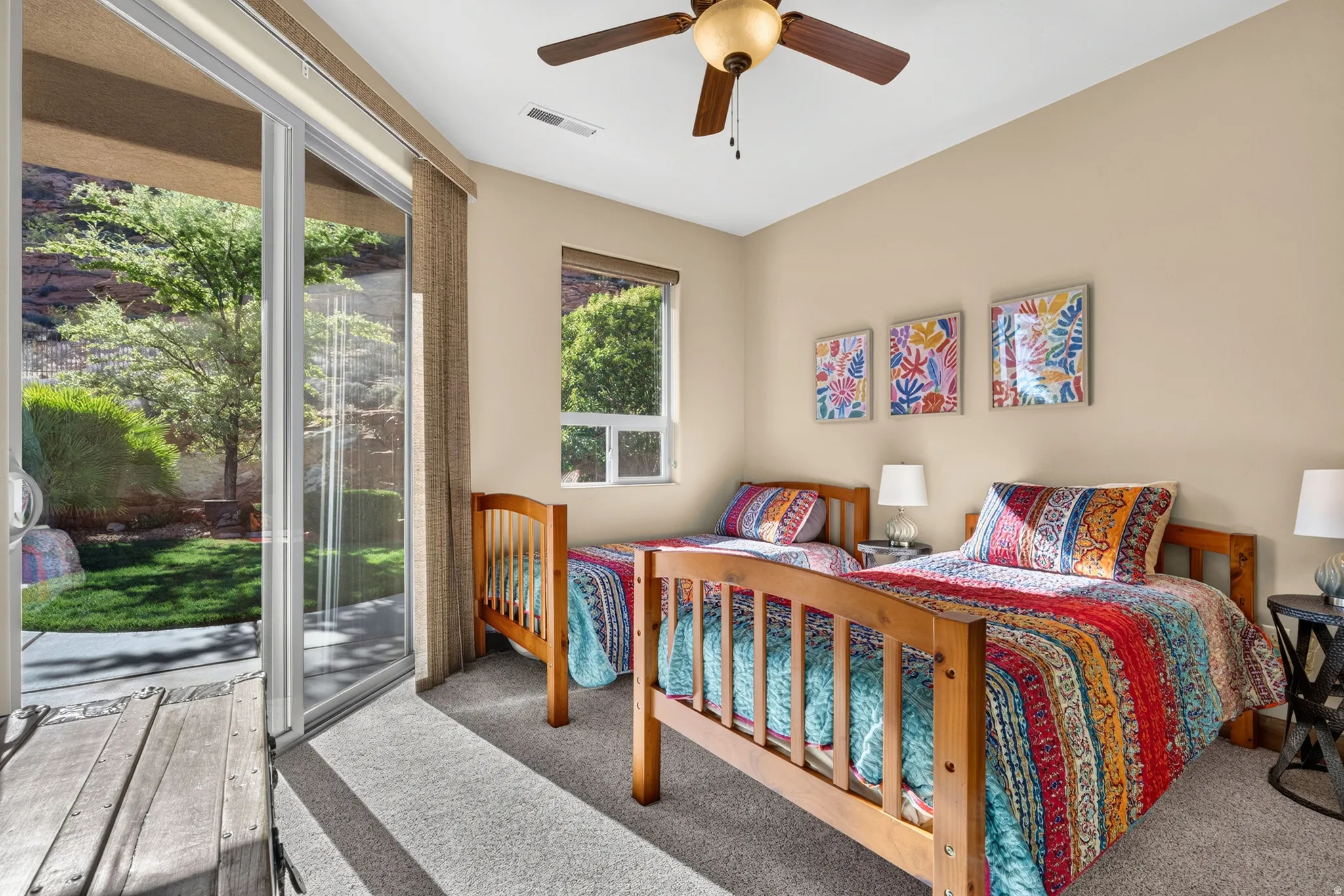 Sliding glass door leading to a patio with surrounding foliage, a single window, and a ceiling fan
