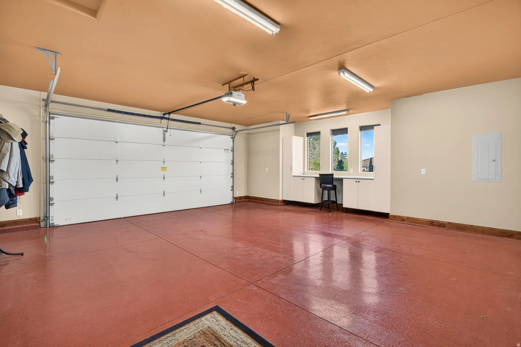 Spacious garage featuring a large automatic garage door, built-in cabinetry with a desk area, multiple windows, and overhead fluorescent lighting
