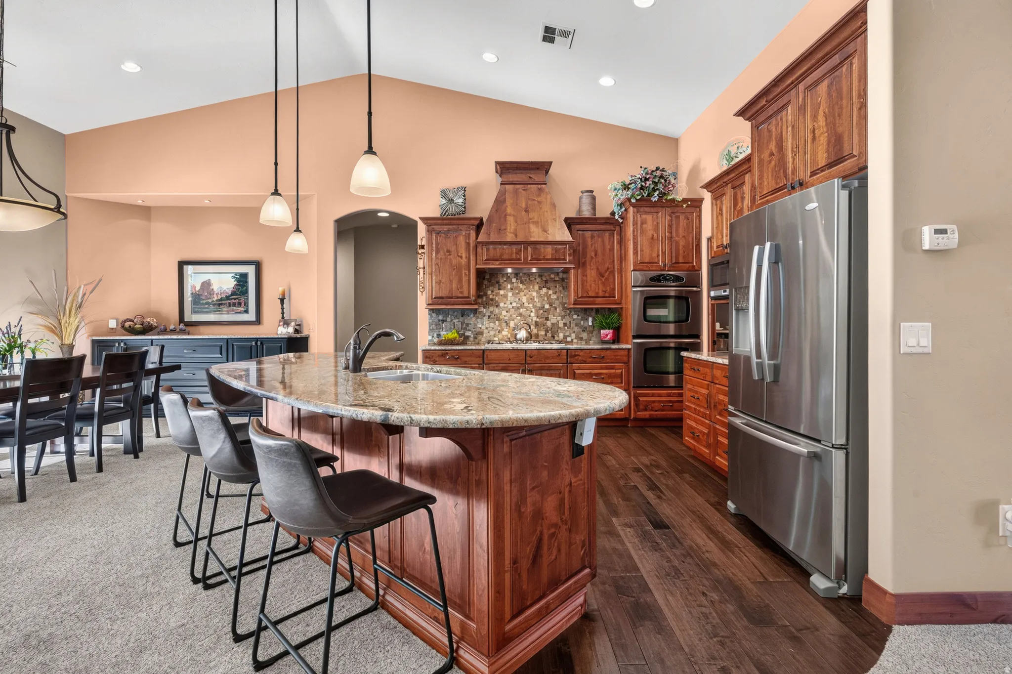 Kitchen featuring wood-finish cabinetry, granite countertops, stainless steel appliances, a center island with sink, and wood-finish flooring