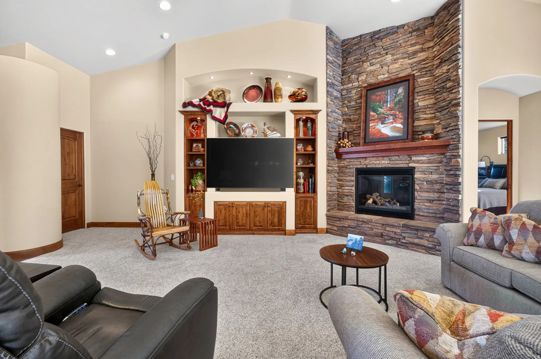 Vaulted ceiling, stone-clad fireplace with mantel, built-in entertainment center, recessed lighting, and wood-paneled doors