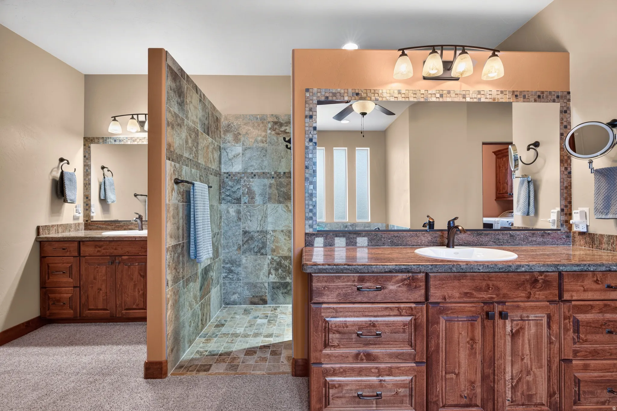 Dual wood-finish vanities with undermount sinks, stone-finish countertops, and mosaic tile accents
