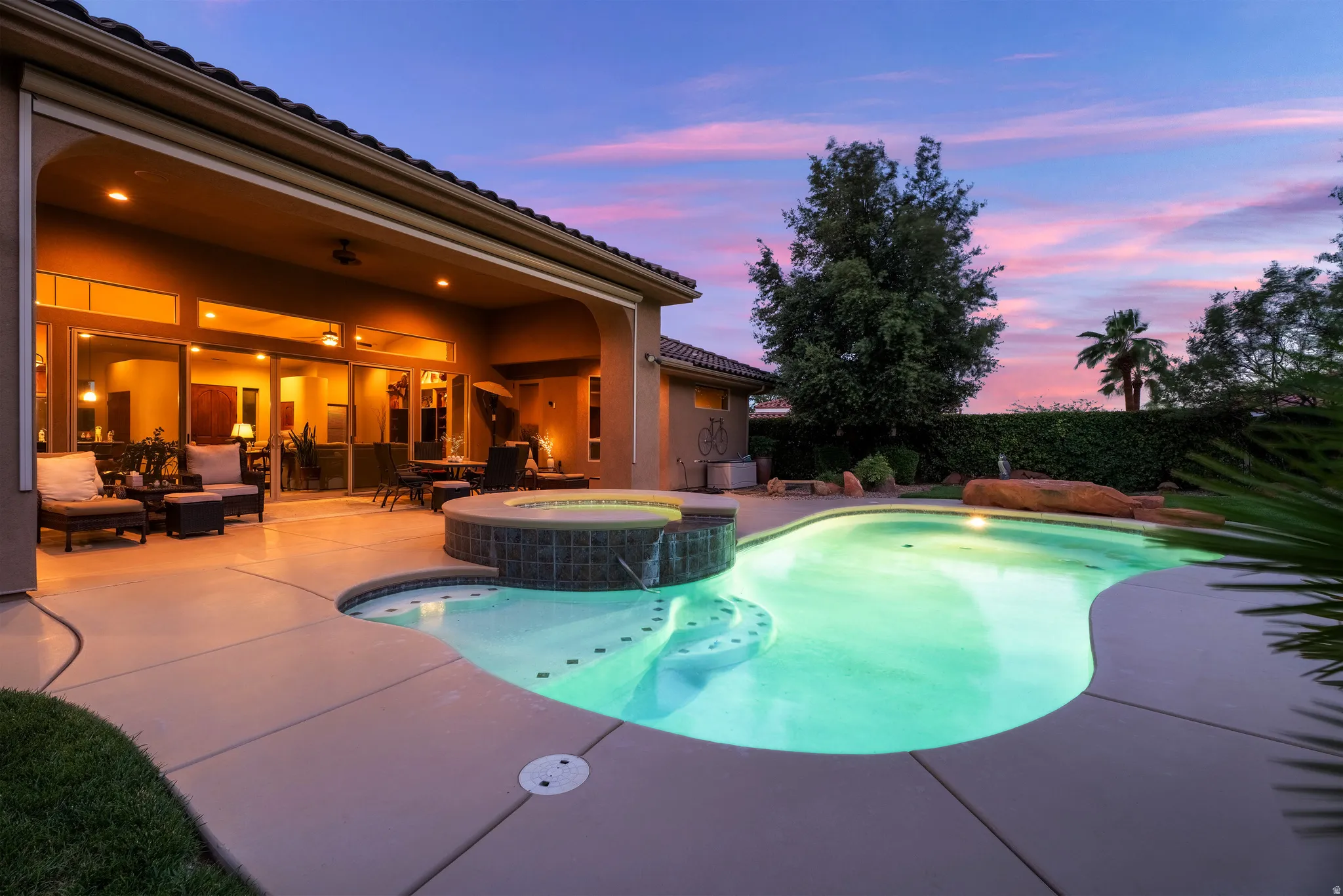 Resort-style backyard featuring a freeform swimming pool, integrated spa with tile surround, and covered patio with multiple sliding glass doors