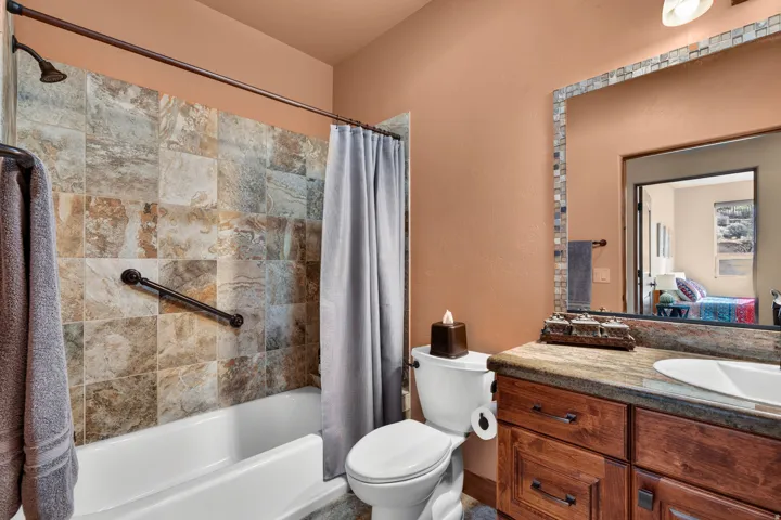 Tub/shower combination with tile surround, wood-finish vanity with countertop, and framed mirror