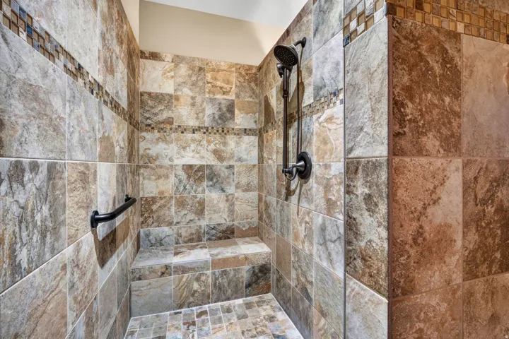 Walk-in shower with natural stone-look tile, mosaic tile accent, built-in bench, and black grab bar