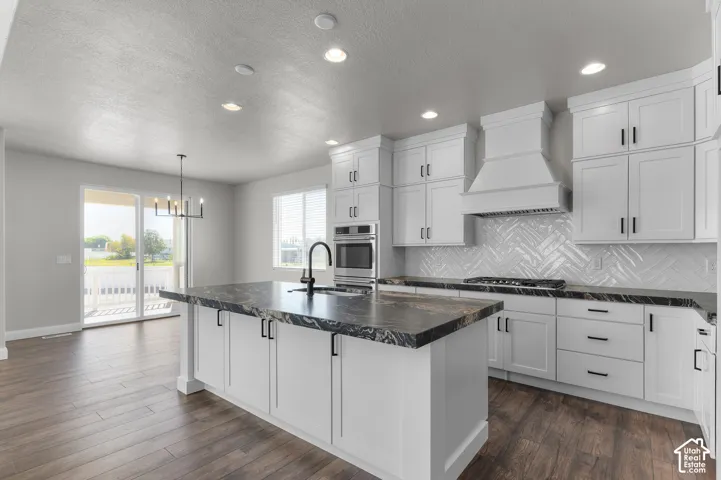 Kitchen featuring white Shaker-style cabinetry, dark stone-finish countertops, a herringbone-pattern tile backsplash, built-in double ovens, and wood-finish flooring