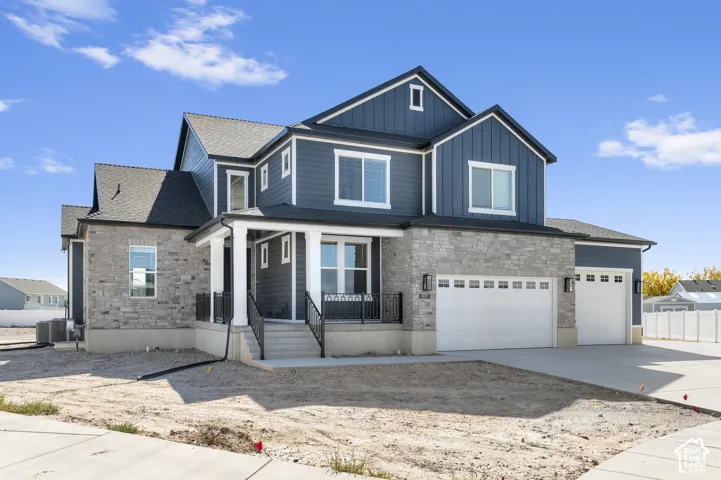 Multi-story exterior featuring blue vertical and horizontal siding, stone veneer masonry, a covered front porch with white columns, and a three-car garage