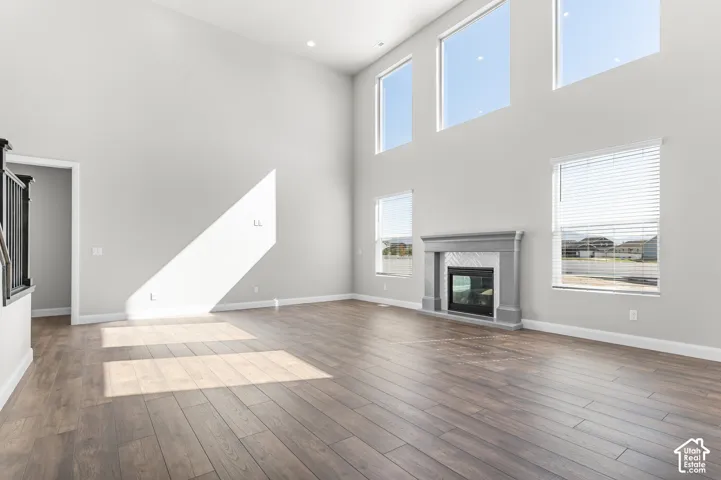 Expansive room featuring soaring ceilings, wood-finish flooring, multi-level windows, and a fireplace with a masonry-style surround