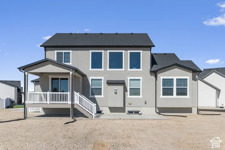 Two-story exterior featuring light-toned stucco siding, high-contrast roof shingles, a raised composite deck with white railings, and large pane windows