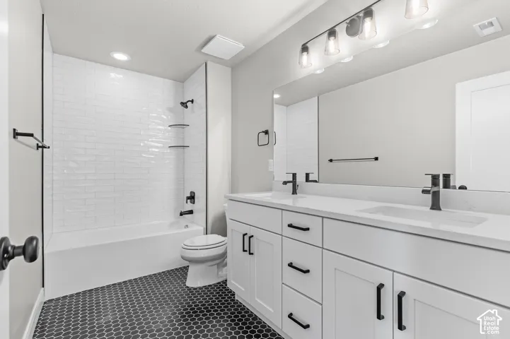 Dual-sink vanity with a solid-surface countertop, white shaker-style cabinetry, matte black hardware, floor-to-ceiling white subway tile shower surround, and hexagonal tile flooring