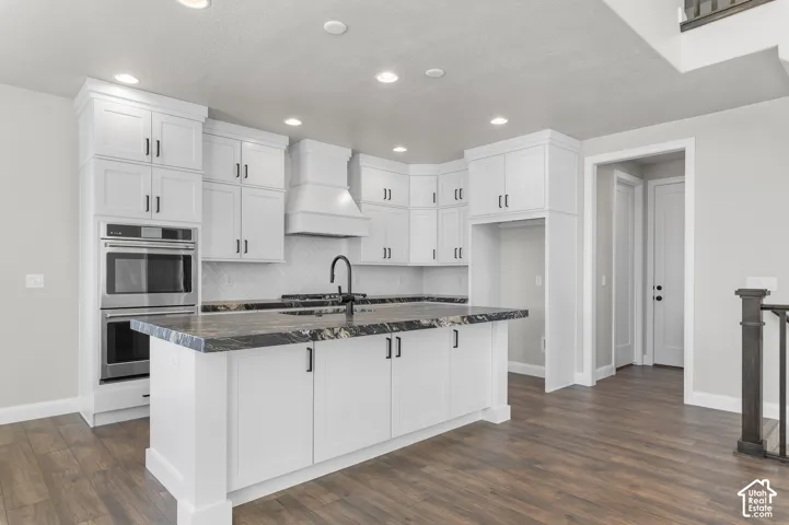 Kitchen featuring white cabinetry with matte black hardware, stone-surface countertops, wood-finish flooring, built-in double ovens, and a herringbone-patterned tile backsplash