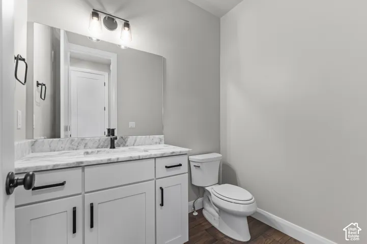 White cabinetry vanity featuring a natural stone countertop, integrated sink, matte black hardware, and dual-light fixture, paired with dark wood-finish flooring