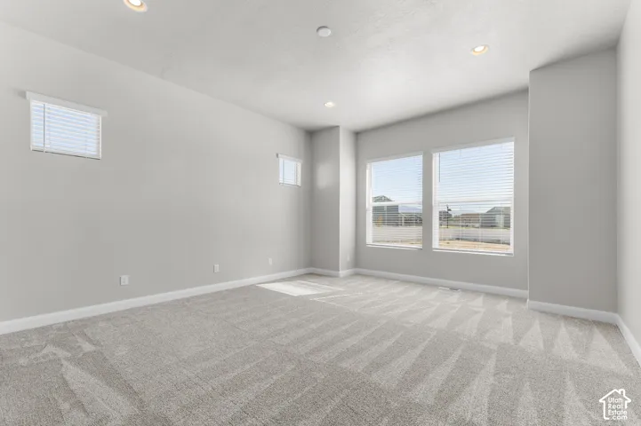 Neutral-toned interior space featuring light-colored wall-to-wall carpeting, recessed ceiling lighting, and multiple windows with horizontal blinds