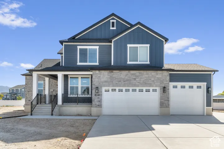 Two-story exterior featuring a mix of vertical siding and stone veneer, a covered front porch with iron railings, and a three-car garage
