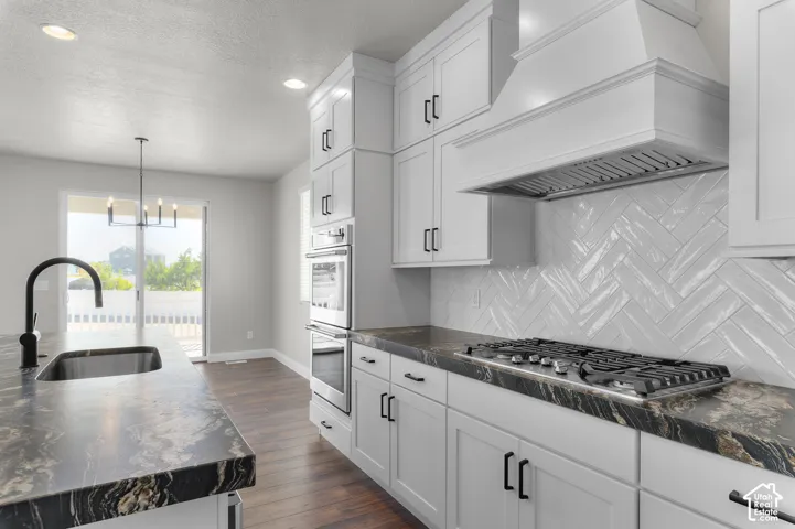 Kitchen featuring white cabinetry, dark stone-finish countertops, herringbone-pattern tile backsplash, stainless steel built-in double oven, and gas cooktop