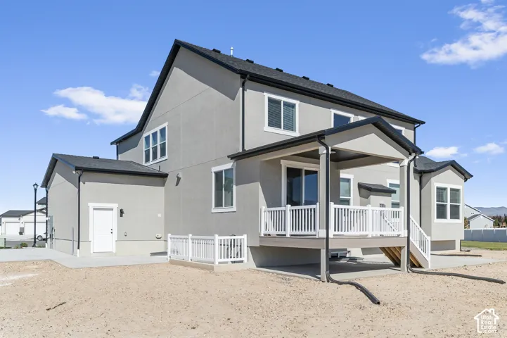 Stucco exterior featuring a covered rear deck with white railing, concrete patio, asphalt shingle roof, and sliding glass door