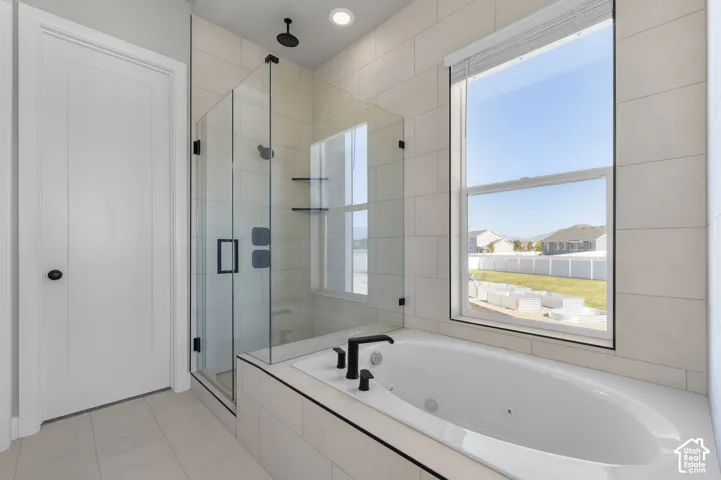 Bathroom featuring a jetted soaking tub, glass-enclosed shower, matte black plumbing fixtures, and large-format tile wall surround