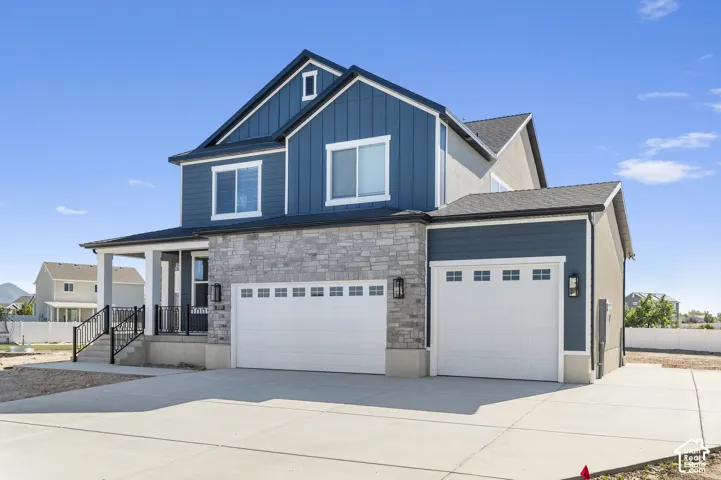 Multi-story residence featuring vertical and horizontal siding, stone veneer masonry, a multi-car garage, and a covered front porch with iron railings
